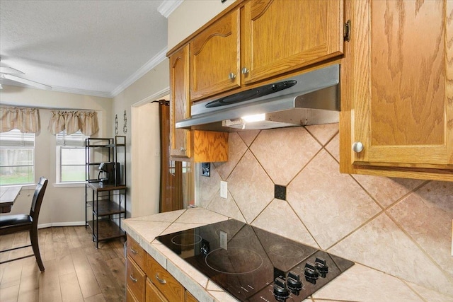 kitchen featuring tasteful backsplash, black electric cooktop, crown molding, and tile countertops