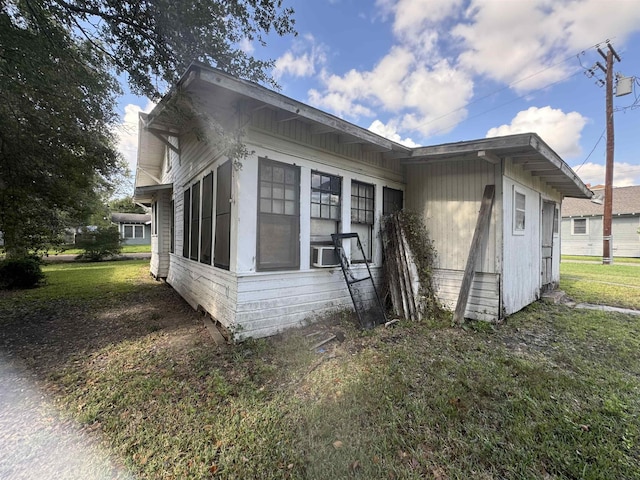 view of property exterior featuring a lawn, cooling unit, and a sunroom