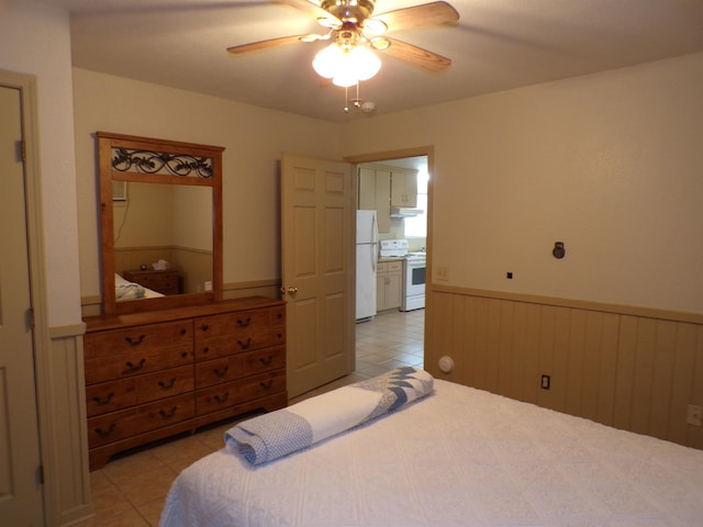 bedroom featuring freestanding refrigerator, wainscoting, ceiling fan, and light tile patterned flooring