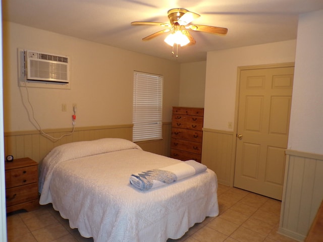 bedroom with a wall mounted AC, ceiling fan, light tile patterned flooring, and wainscoting