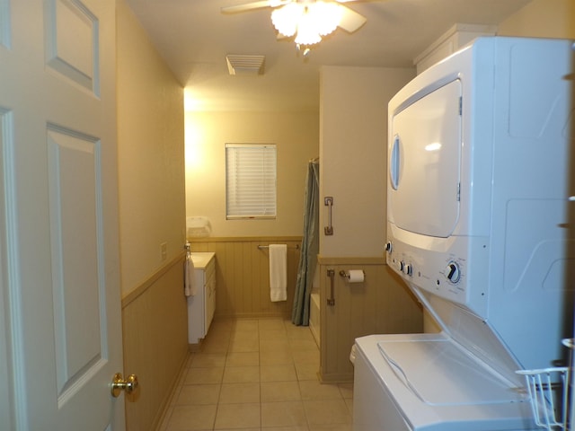 washroom featuring light tile patterned floors, visible vents, stacked washer and clothes dryer, a wainscoted wall, and ceiling fan