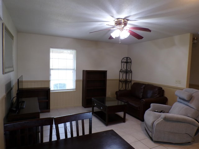 living room with a wainscoted wall, a ceiling fan, and light tile patterned flooring