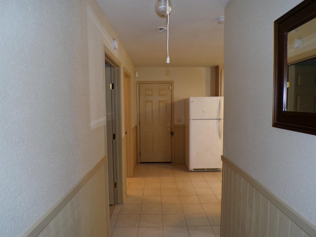 hall featuring a wainscoted wall, a textured wall, and light tile patterned flooring