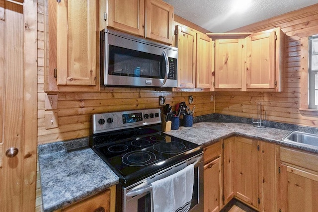 kitchen with sink, wooden walls, a textured ceiling, light brown cabinetry, and stainless steel appliances