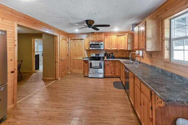 kitchen featuring wood walls, sink, light hardwood / wood-style flooring, ceiling fan, and stainless steel appliances