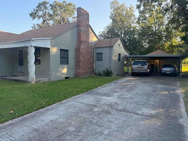 view of side of property with a lawn, driveway, roof with shingles, a carport, and a chimney