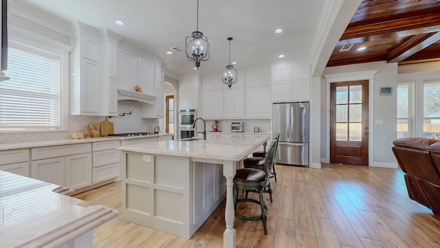 kitchen featuring light hardwood / wood-style floors, pendant lighting, a center island with sink, white cabinetry, and stainless steel appliances