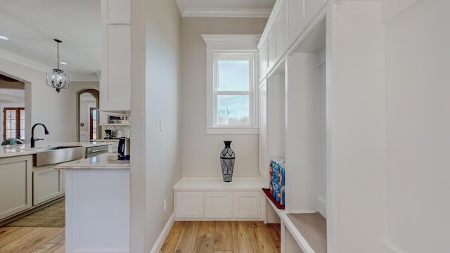 kitchen with white cabinets, sink, hanging light fixtures, ornamental molding, and light hardwood / wood-style flooring