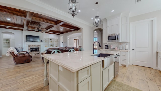 kitchen featuring wood ceiling, a center island with sink, a brick fireplace, appliances with stainless steel finishes, and hanging light fixtures