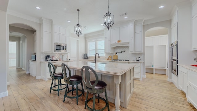 kitchen with pendant lighting, white cabinets, stainless steel appliances, a breakfast bar, and a center island with sink