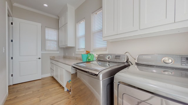 clothes washing area with cabinets, washer and dryer, ornamental molding, and light hardwood / wood-style flooring