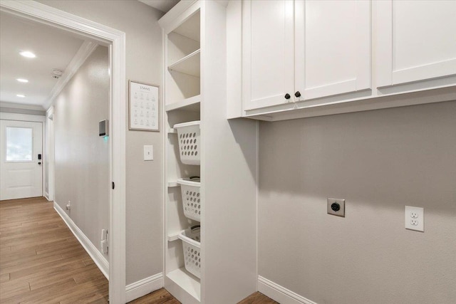 washroom featuring electric dryer hookup, crown molding, light hardwood / wood-style flooring, and cabinets