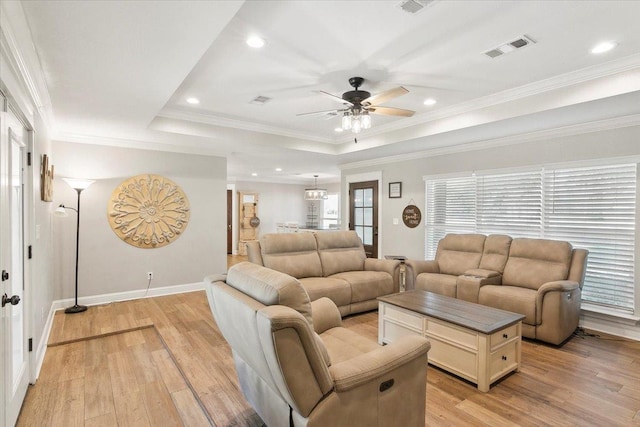 living room featuring a raised ceiling, ceiling fan, ornamental molding, and light wood-type flooring