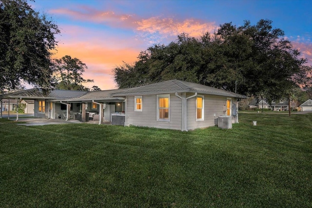 back house at dusk with a lawn and central AC unit