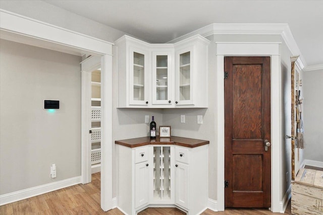 bar with light hardwood / wood-style floors, white cabinetry, and crown molding