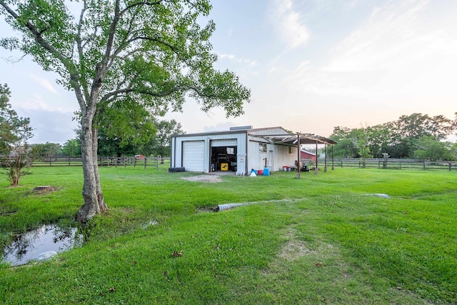 yard at dusk featuring a rural view, a garage, and an outdoor structure