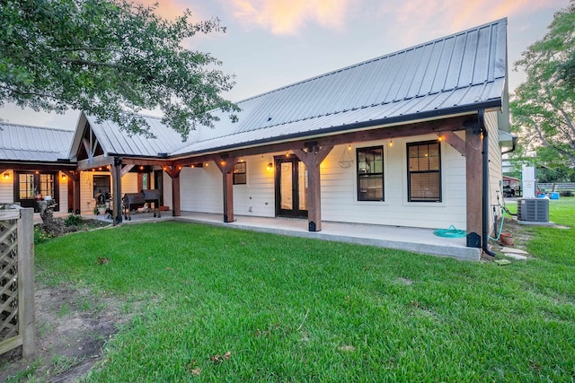 back house at dusk featuring a yard, central AC, and a patio area