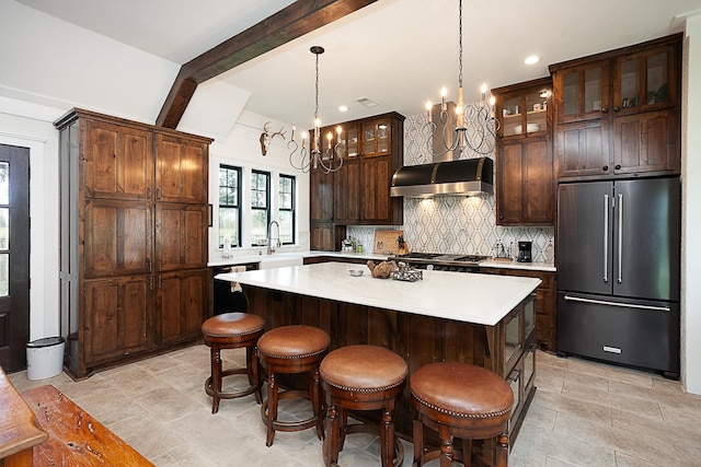 kitchen featuring stainless steel fridge, wall chimney range hood, beamed ceiling, a chandelier, and a kitchen island