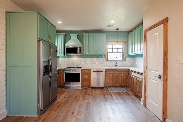 kitchen featuring backsplash, sink, light wood-type flooring, decorative light fixtures, and stainless steel appliances