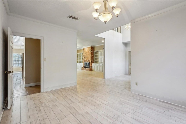 empty room featuring ornamental molding, light wood-style flooring, a fireplace, and visible vents