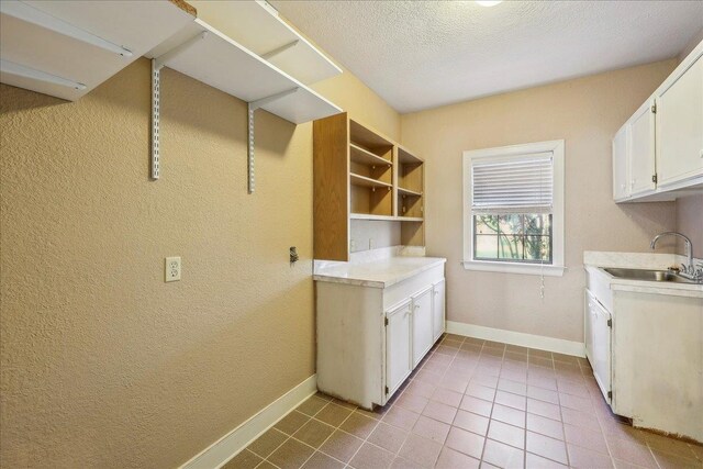 washroom with baseboards, a textured ceiling, a sink, and tile patterned floors