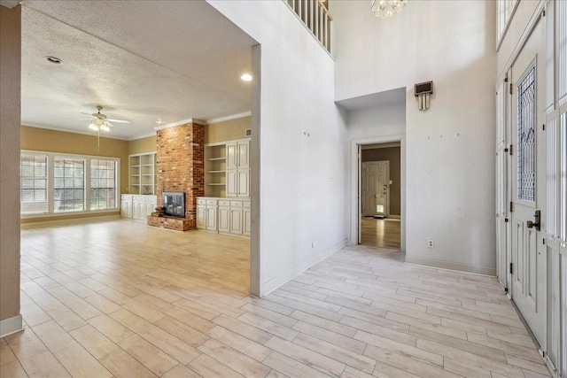 entryway with a textured ceiling, ceiling fan with notable chandelier, a fireplace, baseboards, and light wood-style floors