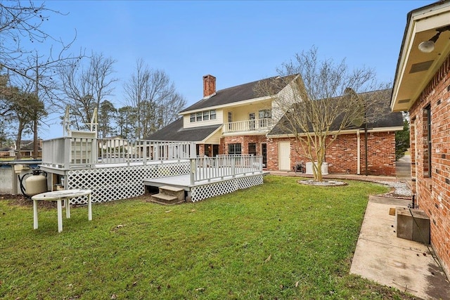 back of property with a deck, brick siding, a chimney, and a lawn