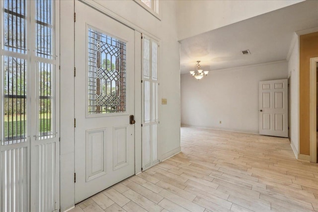 entryway with a notable chandelier, a towering ceiling, baseboards, visible vents, and light wood finished floors