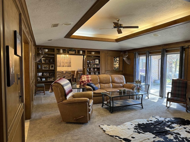 carpeted living room with a raised ceiling, ceiling fan, built in features, and a textured ceiling