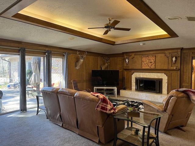 living room with a textured ceiling, ceiling fan, a raised ceiling, and light carpet