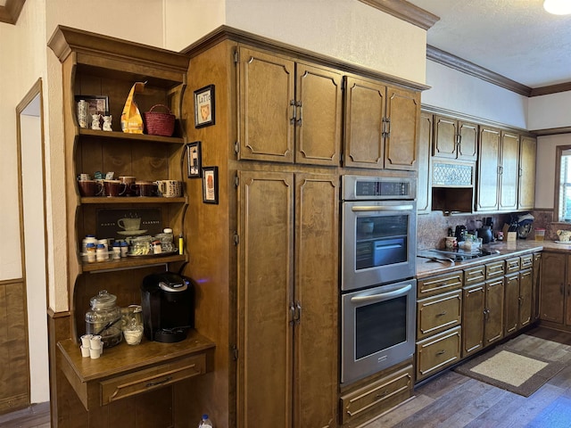 kitchen featuring dark wood-type flooring, stainless steel double oven, gas stovetop, decorative backsplash, and ornamental molding