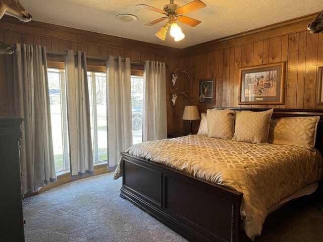 bedroom with carpet, ceiling fan, wooden walls, and multiple windows