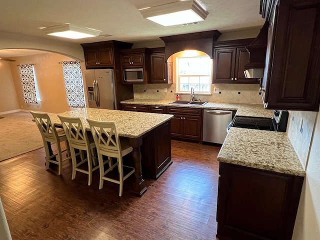 kitchen featuring decorative backsplash, appliances with stainless steel finishes, a breakfast bar, sink, and a center island