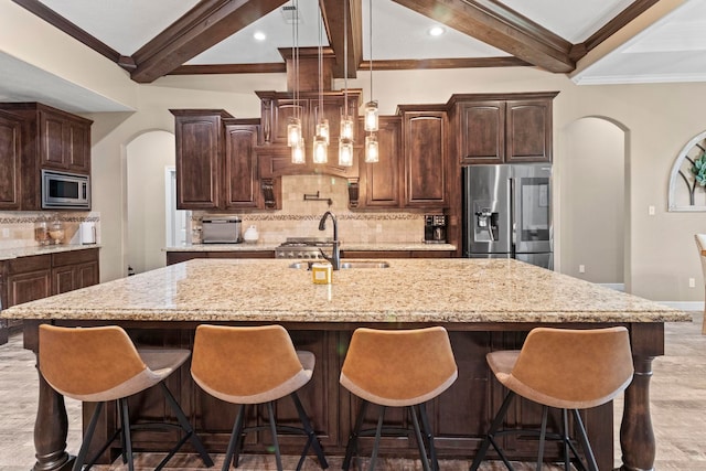 8395 Carrie Ln, Beaumont, TX 77713 - kitchen featuring arched walkways, beamed ceiling, stainless steel appliances, an island with sink, and tasteful backsplash