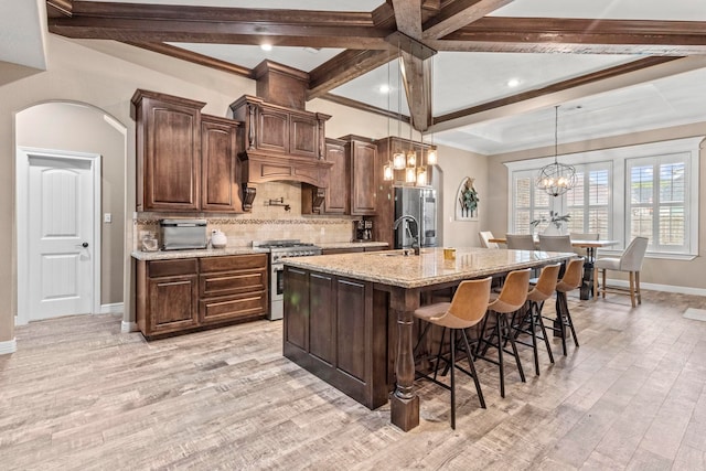 8395 Carrie Ln, Beaumont, TX 77713 - kitchen featuring arched walkways, appliances with stainless steel finishes, light wood-style flooring, an island with sink, and a kitchen breakfast bar
