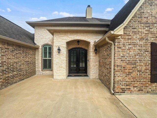 entrance to property with brick siding, roof with shingles, and french doors