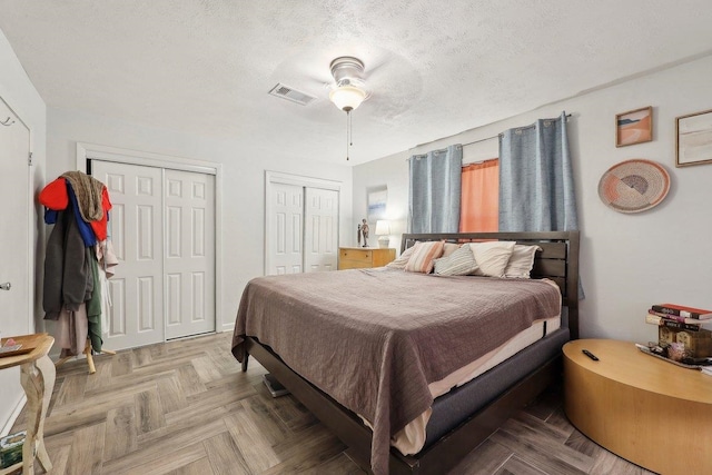 bedroom featuring visible vents, multiple closets, a textured ceiling, and a ceiling fan