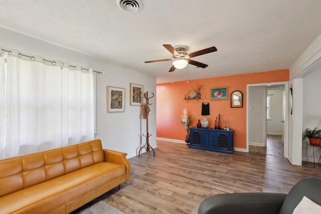 living room featuring a ceiling fan, visible vents, light wood finished floors, and baseboards