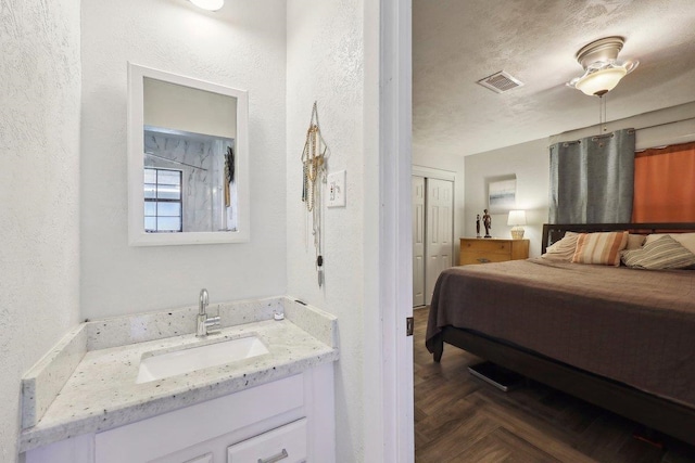 bedroom with a textured wall, visible vents, a closet, and a sink