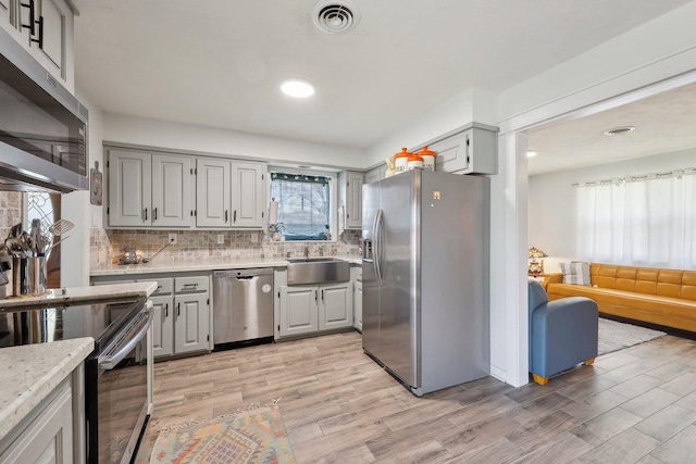 kitchen featuring visible vents, gray cabinets, a sink, appliances with stainless steel finishes, and backsplash