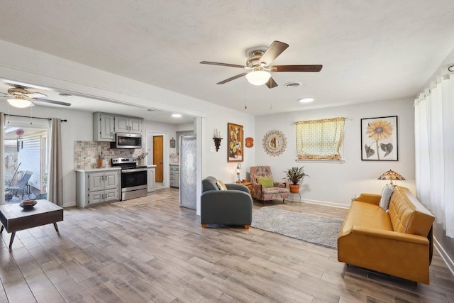 living area featuring visible vents, baseboards, a ceiling fan, and light wood finished floors