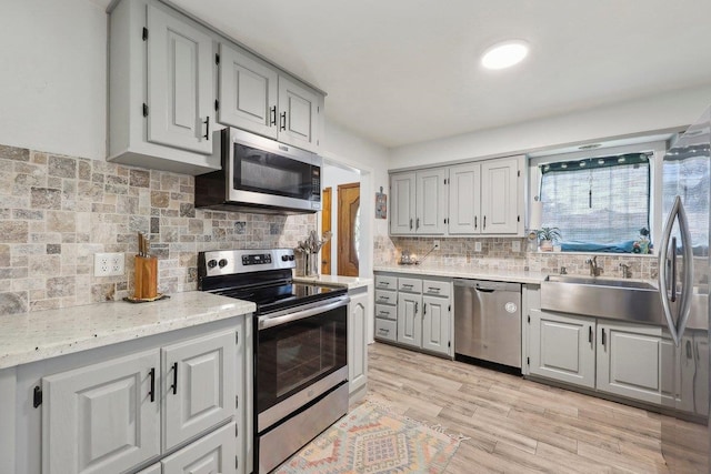 kitchen with light stone counters, light wood-style flooring, gray cabinets, appliances with stainless steel finishes, and backsplash