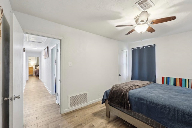 bedroom with visible vents, baseboards, attic access, and light wood finished floors