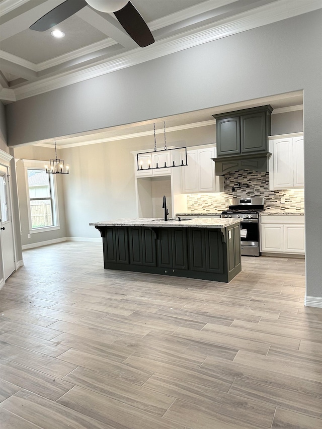 kitchen featuring stainless steel range with gas cooktop, decorative light fixtures, a kitchen island with sink, white cabinets, and light wood-type flooring