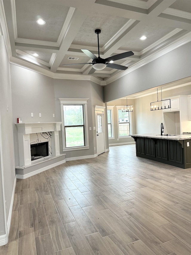 unfurnished living room with coffered ceiling, ceiling fan with notable chandelier, beam ceiling, a premium fireplace, and light hardwood / wood-style floors