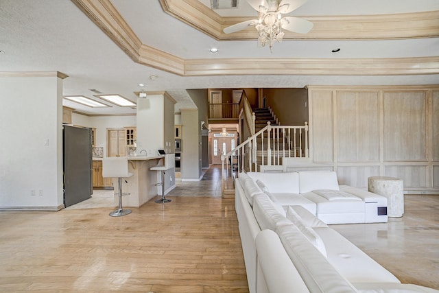 living room featuring ceiling fan, sink, a raised ceiling, crown molding, and light wood-type flooring