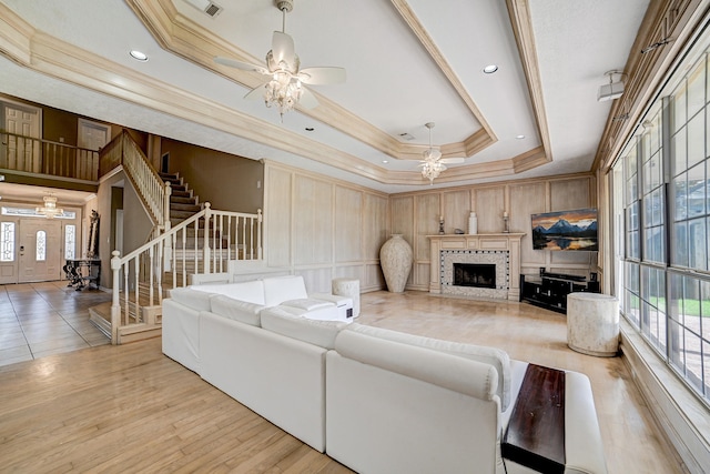 living room featuring a tray ceiling, crown molding, light hardwood / wood-style flooring, and ceiling fan with notable chandelier