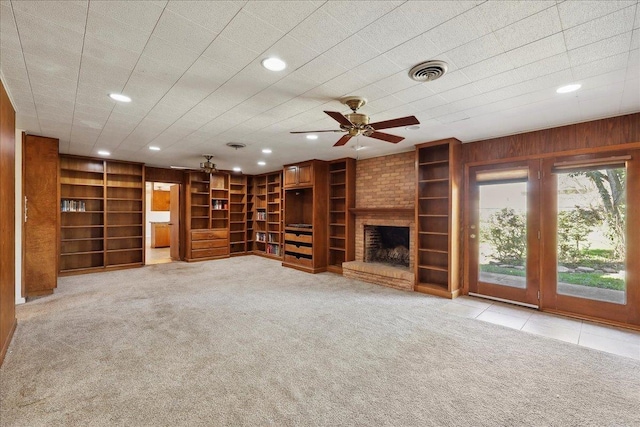 unfurnished living room featuring ceiling fan, visible vents, wood walls, and light carpet