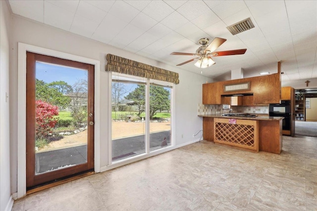 kitchen featuring brown cabinetry, visible vents, a peninsula, ceiling fan, and decorative backsplash