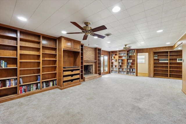 unfurnished living room with visible vents, a ceiling fan, carpet floors, wooden walls, and a fireplace